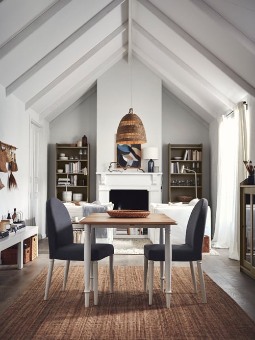 A dining room featuring a rectangular drop leaf table made of wood and steel, next to 2 grey chairs and 2 high cabinets.