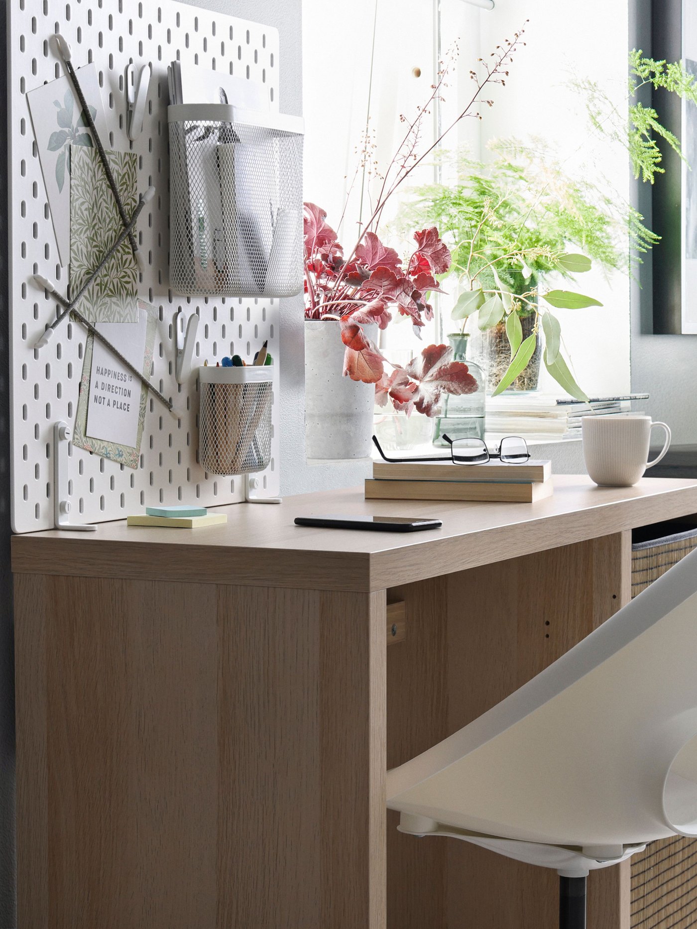 Un escritorio de madera y en la pared del frente un tablero SKÅDIS con organizadores.