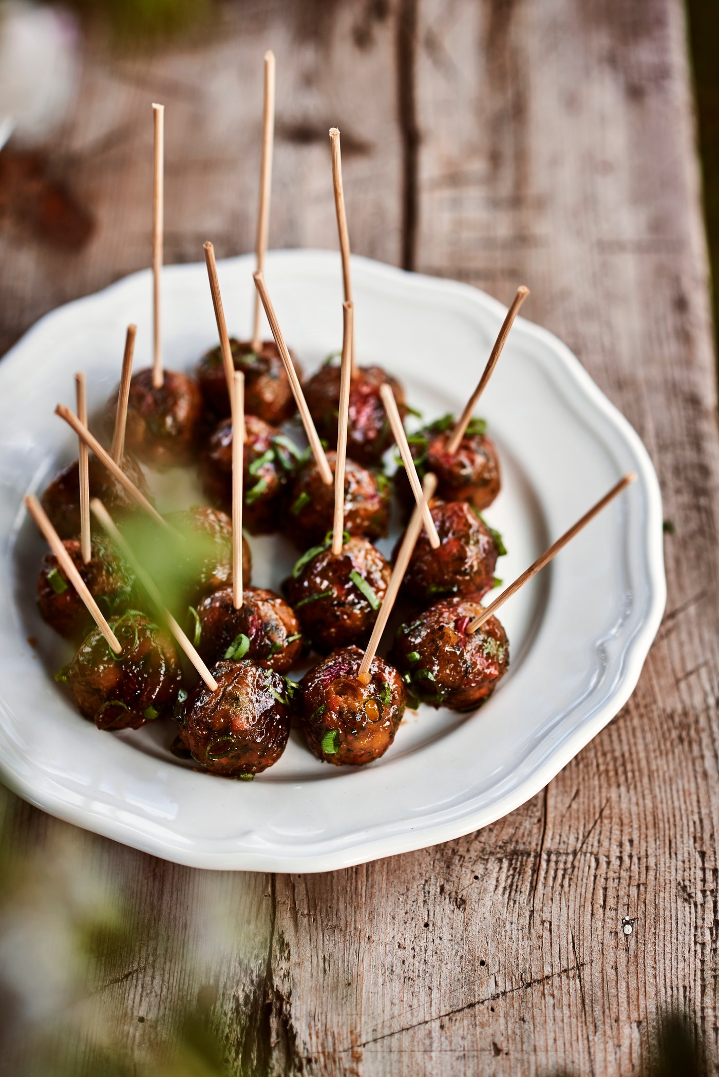 Servierteller mit kleinen Fleischbällchen am Spiess, angerichtet auf weissem Teller auf Holzuntergrund.