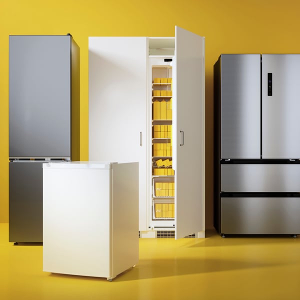 Several fridges and freezers of different sizes and models are placed against a bright yellow-orange background.