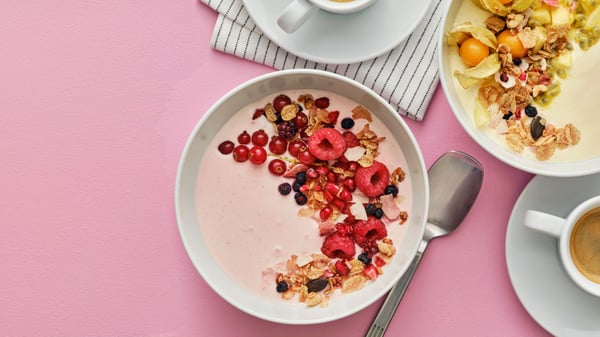 A white bowl has a mix of LÅNGLUR fruit smoothie and yoghurt with HJÄLTEROLL granola and it’s decorated with red berries.