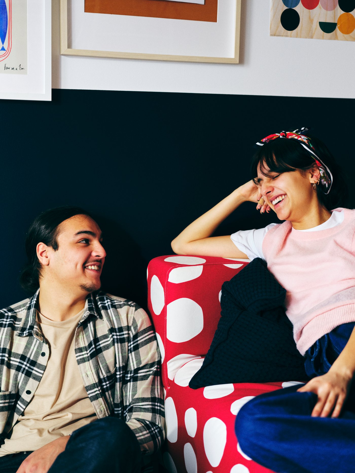 A man and a woman smile at each other, one seated in a red-and-white KLIPPAN two-seat sofa, the other on the floor beside.