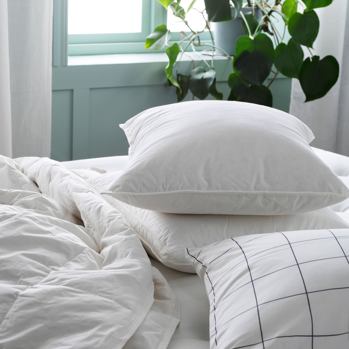 Two pillows without pillowcases on top of each other on a bed beside an uncovered duvet and another pillow in a case.