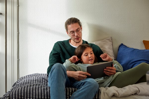 Un père et sa fille regardent une tablette électronique, assis ensemble sur le canapé.