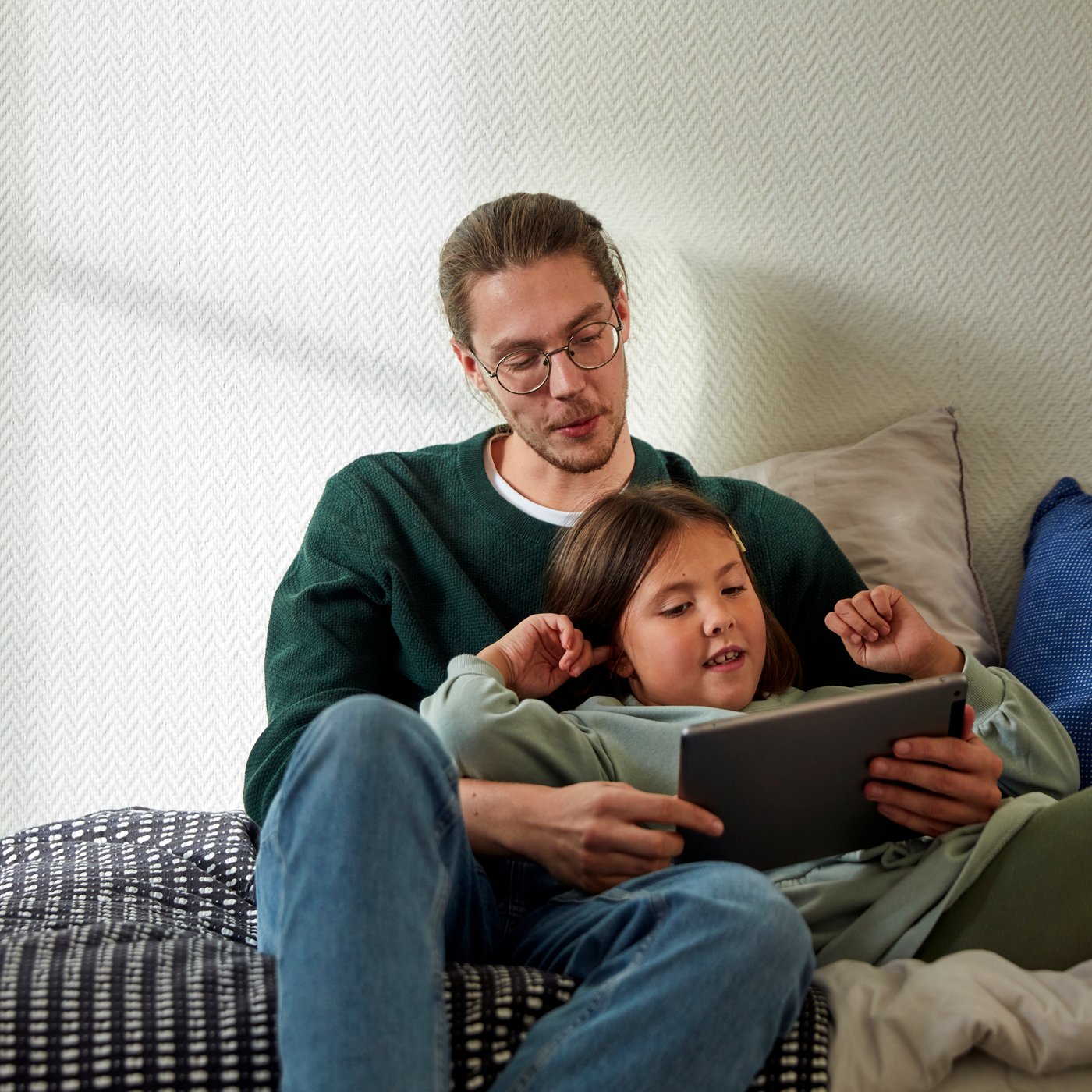 A person sitting on a bed with a child looking at a tablet