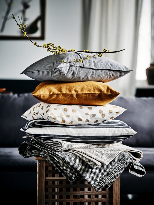 Textiles and stacked cushions, with golden-brown VIGDIS and white-and-gold SKÄGGÖRT cushion covers, on a HOL side table.