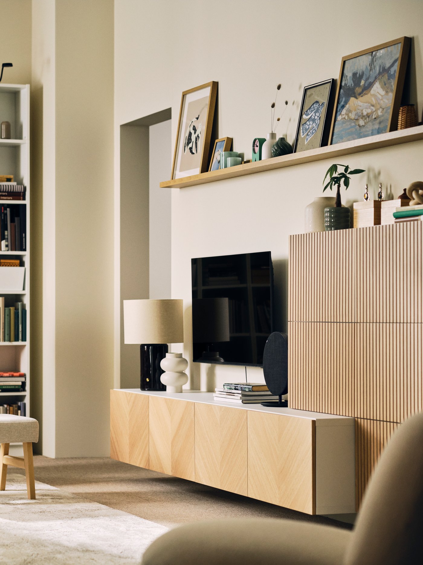 Un salon soigné et lumineux, aménagé avec un ensemble de rangements BESTÅ aux façades en placage de chêne, des étagères et un fauteuil EKENÄSET.