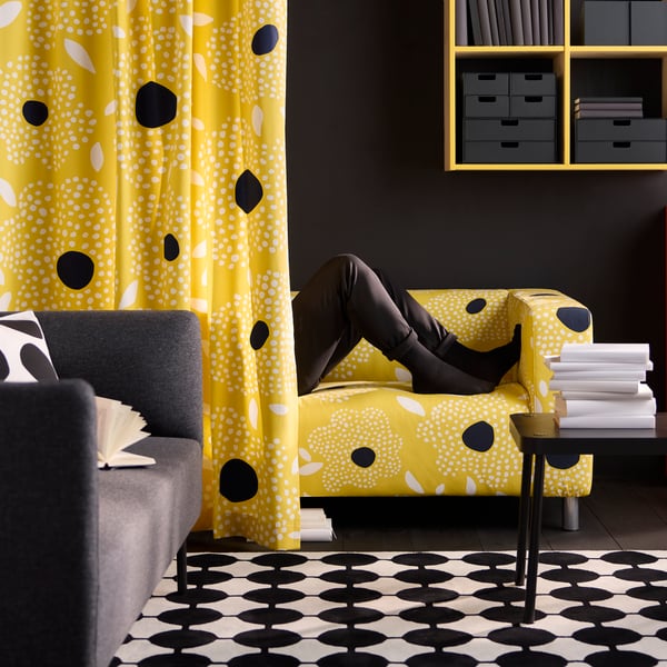 A curtain made of yellow, black, and white pre-cut BUSKOPUNTIA fabric with a dot pattern hangs in front of a sofa.