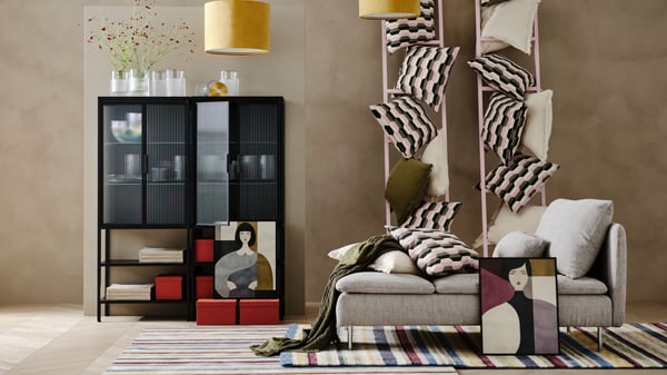 Two MOSSJÖN glass-door cabinets with RÄFFELBJÖRK and PÅDRAG vases inside the cabinets. A BÅTSPINNARE cushion cover leans against TANDMOTT, SANELA and VALLKRASSING cushion covers on a SÖDERHAMN chaise longue.