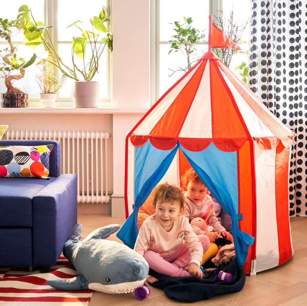 2 young children sit in the red / blue / white strip design CIRKUSTÄLT child tent in the living room.