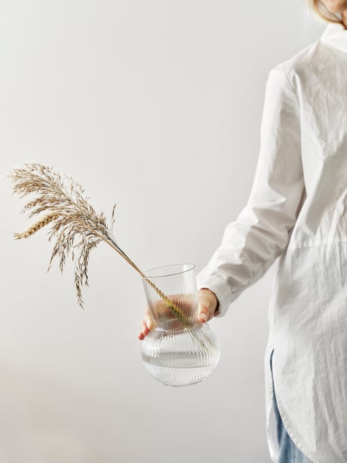 A model holding the PÅDRAG in her hand. The vase has some dried wheat in in.