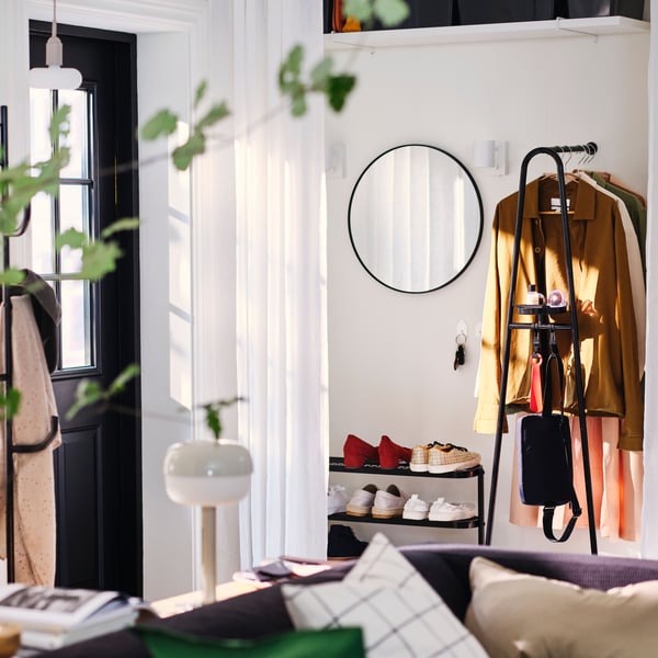 A bright living room with an entryway in a corner which has a black ÄLGANÄS hat/coat stand on one side of the front door.