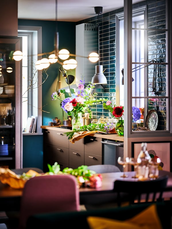 Una cocina con alacenas SEKTION y barra de laminado efecto roble SÄLJAN, una lámpara STORSLINGA y un arreglo floral.