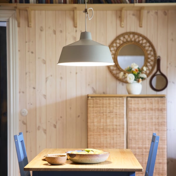 A SJÖMAKT pendant lamp lights up a PINNTORP table that has a GLADELIG serving bowl and a bowl on top of it.