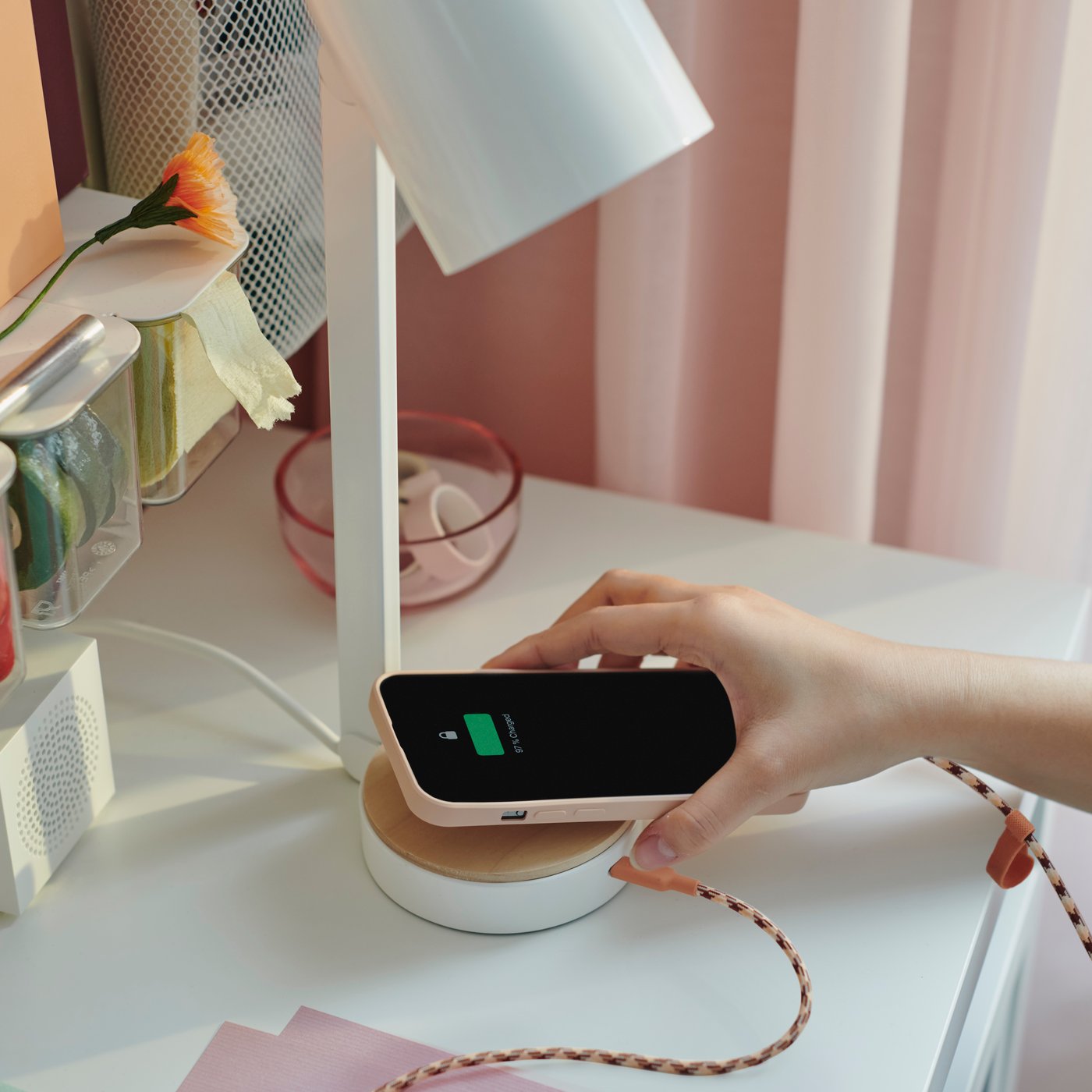 Main tenant un smartphone relié par un câble au port USB-C situé dans le pied d’une lampe de bureau ENSMÄRKE.