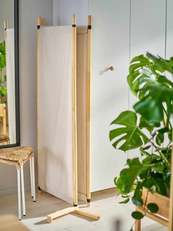 La cloison GLAMBERGET en bois brut et textile beige est repliée à côté des armoires PLATSA blanches.