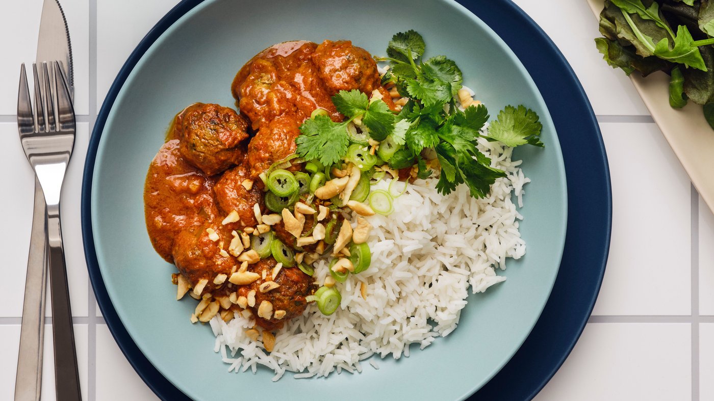 A turquoise plate is placed on top of a blue plate and contains rice and a stew and is garnished with coriander.