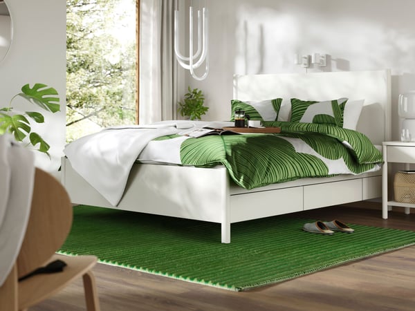 Groen vloerkleed TÅGSPÅR onder een wit bed met een groen beddengoed