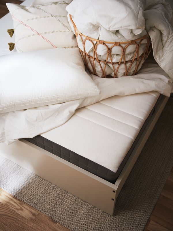 A dark grey MORGEDAL foam mattress on a light beige GURSKEN bed frame, with a rattan basket and various bedding on top.
