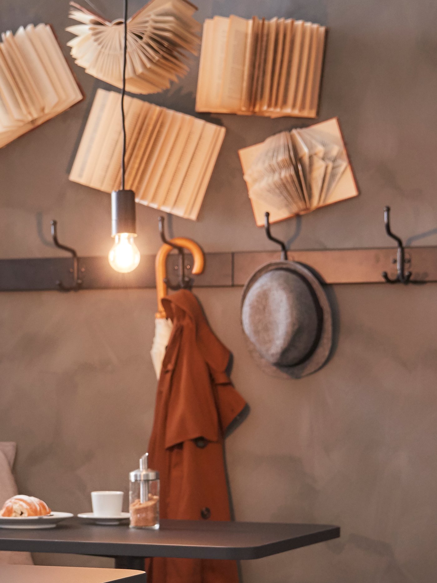 A light bulb with a black cord hanging from the ceiling and a wall rack with hooks and a hat and an umbrella on it.