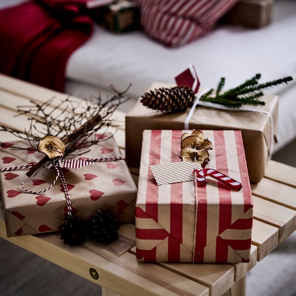 Flera julklappar inslagna i brunt papper med röda hjärtan och ränder, dekorerade med kottar och torkade apelsinskivor.