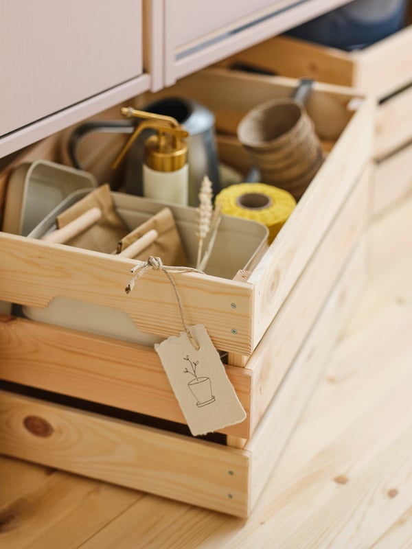 Es sind zwei KNAGGLIG Kästen mit verschiedenen Gegenständen auf dem Boden unter einem IVAR Schrank mit rosa gestrichenen Schiebetüren zu sehen.