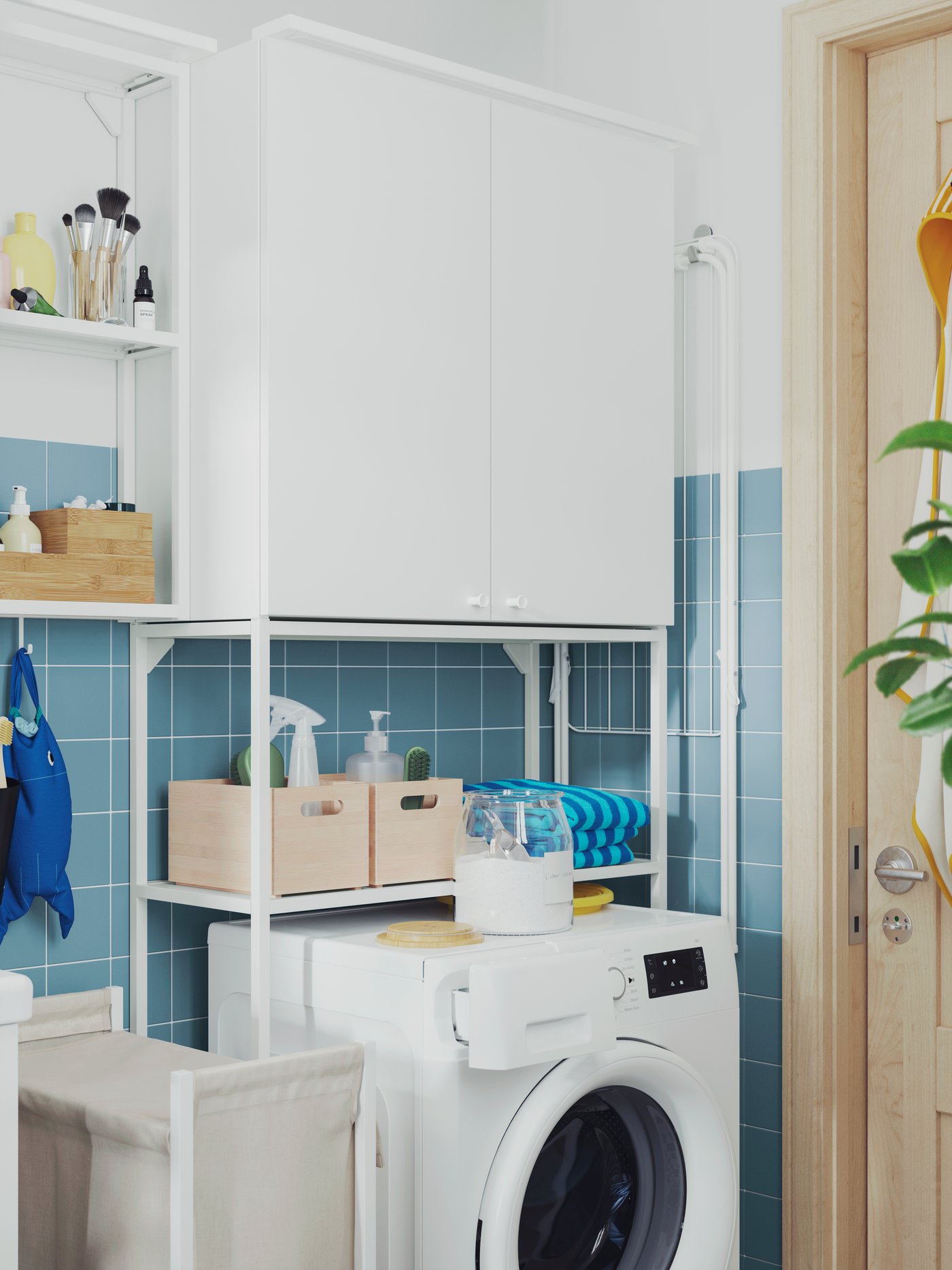 A white ENHET frame with shelves for washing machine is placed above a white washing machine, next to a laundry bag.