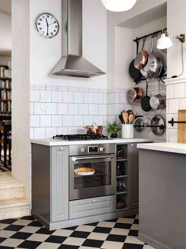 Base cabinets with grey BODBYN kitchen fronts on both sides of a hob and oven, plus black wall rails holding pots and pans.