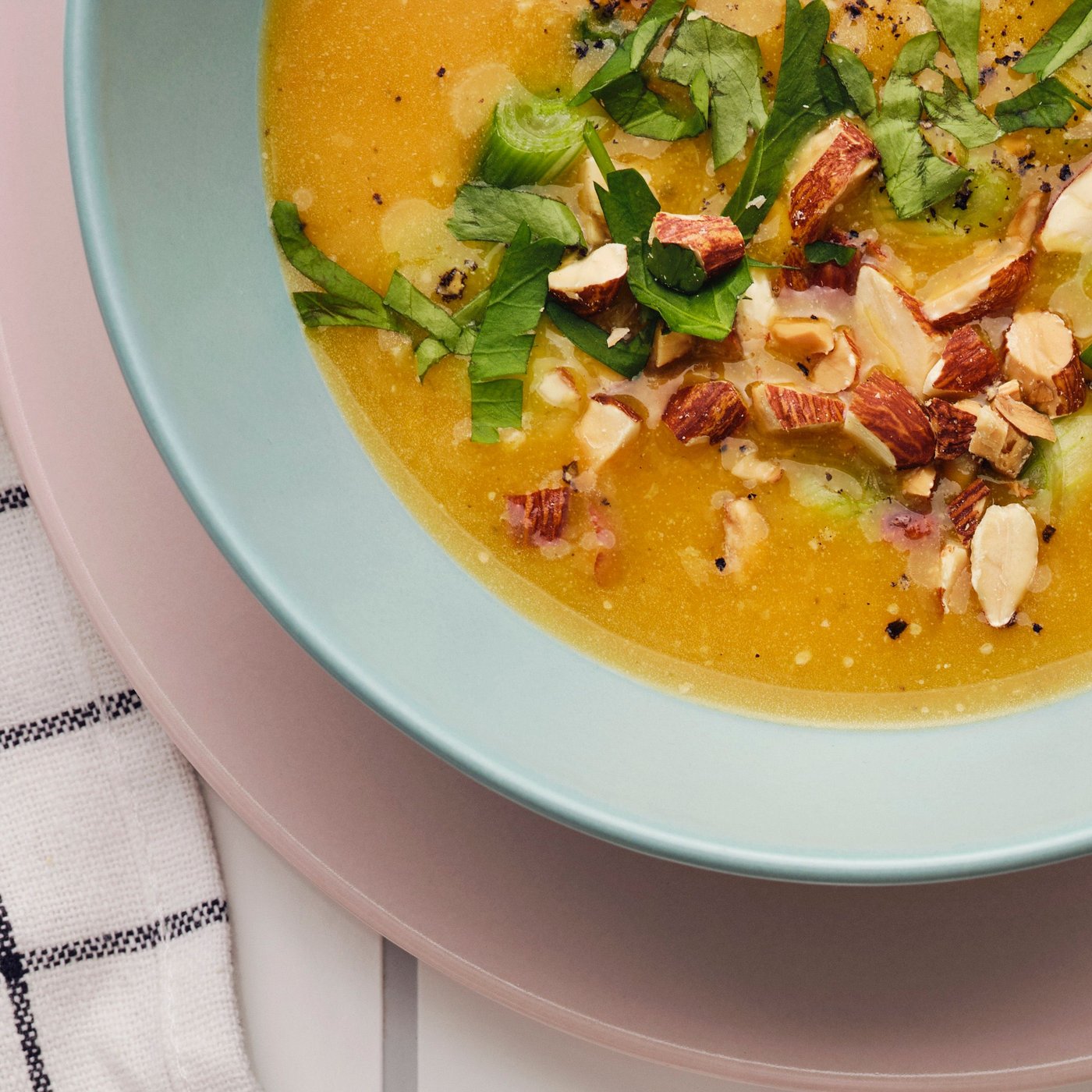 Pumpkin soup with herbs and MUNSBIT roasted almonds served in a blue bowl on top of a pink plate.