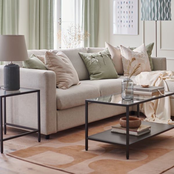A beige VIMLE 3-seat sofa on an orange-red RÖDASK rug with a metal coffee table with glass top in the living room.