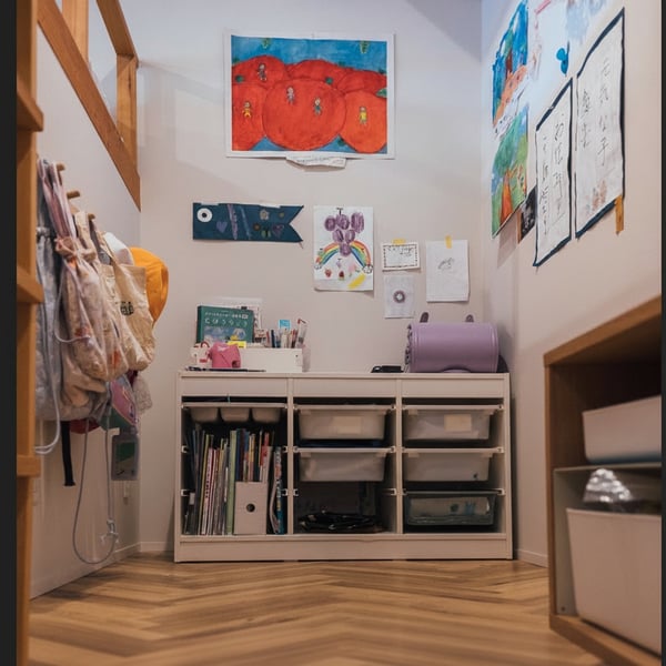 子どもの作品が壁に飾られたスペースに、白い収納とボックス、文房具が並ぶ学習コーナーがある。