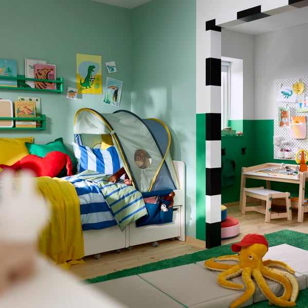An ELDFLUGA bed tent mounted over a children’s bed with bedding and toys in a room with green walls and decorations.