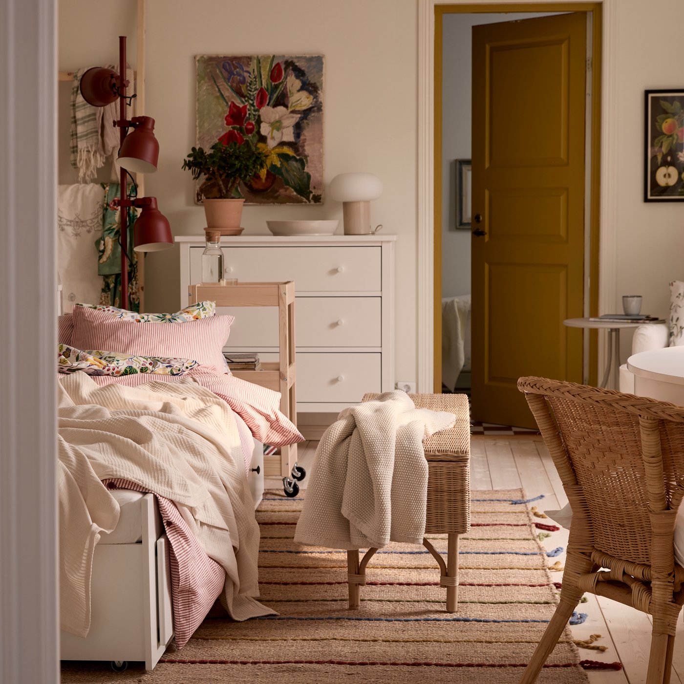 A one-bedroom apartment with HEMNES day-bed, a rattan chair in the foreground and a white HEMNES chest of drawers in the back.