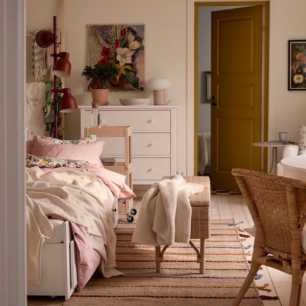 A one-bedroom apartment with HEMNES daybed, a rattan chair in the foreground and a white HEMNES chest of drawers in the back.