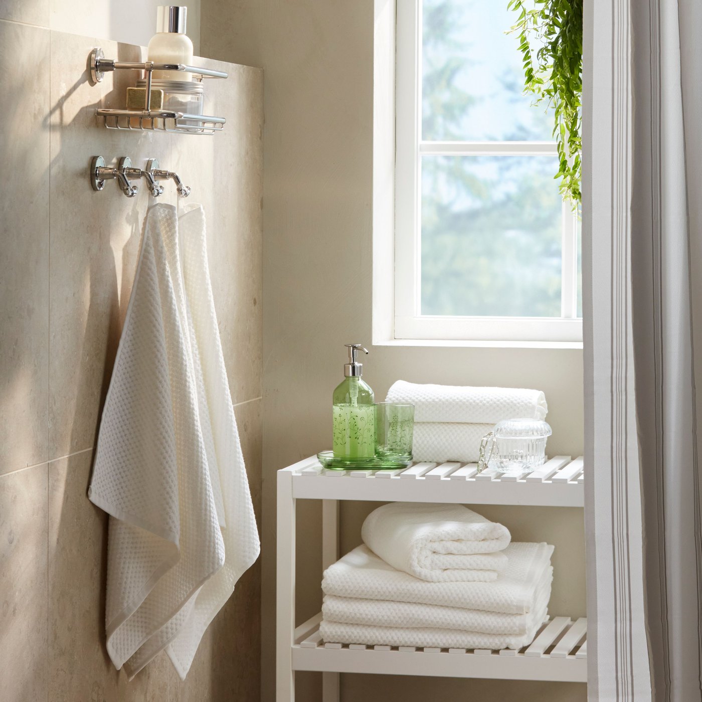 U uglu kupatila nalaze se dva bela GULVIAL peškira za ruke okačena na zidnim kukama pored bele klupe sa naslaganim belim peškirima.