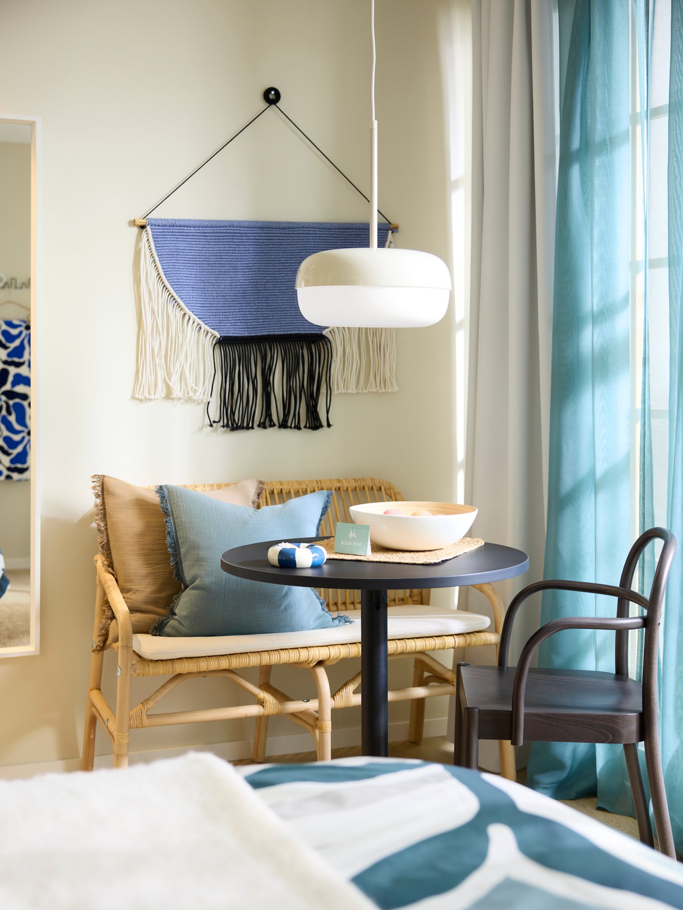 An anthracite STENSELE table with a circular top and bowl of fruit is in the corner of a hotel room by a window and a bench.