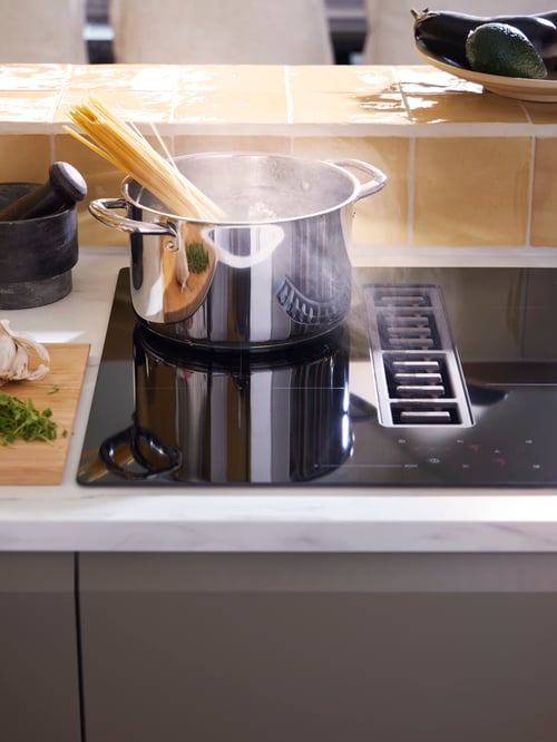 Fotografie parțială a unei plite cu inducție FÖRDELAKTIG de culoare neagră pe care se află un vas de oțel IKEA 365+ care conține fire de paste. 