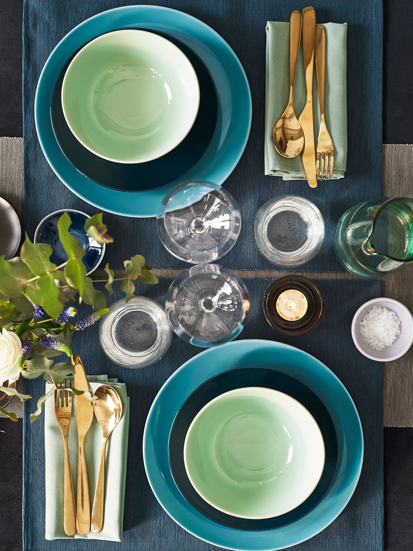 Ein gedeckter Tisch mit goldenem Besteck und türkisen FÄRGRIK Tellern.