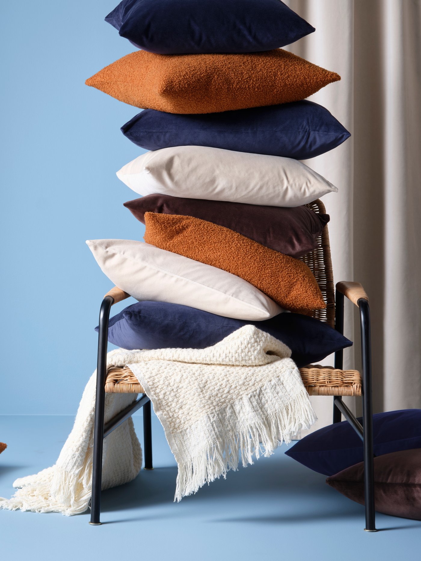 A chair with a stack of cushions & cushion covers in orange, blue and off-white.