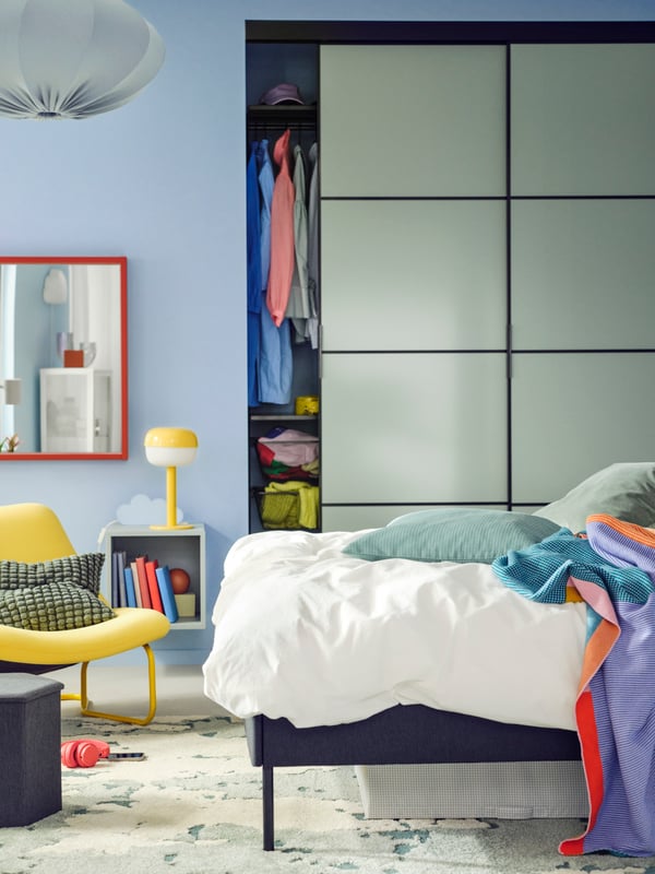 An upholstered bed with ÄNGSLILJA bed linen stands in front of a SKYTTA/BOAXEL reach-in wardrobe with sliding doors.