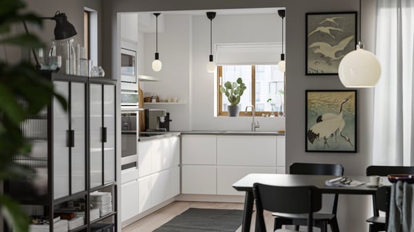 A small kitchen with white walls has smooth white VOXTORP fronts without handles and a dining area with darker furniture.
