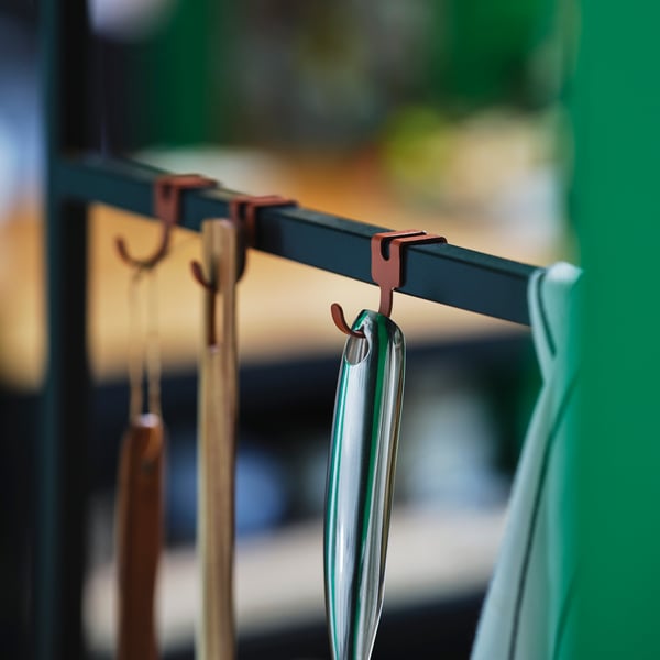 A close-up of various metal and wooden kitchen utensils hanging on reddish hooks in an ÄSPINGE kitchenette.