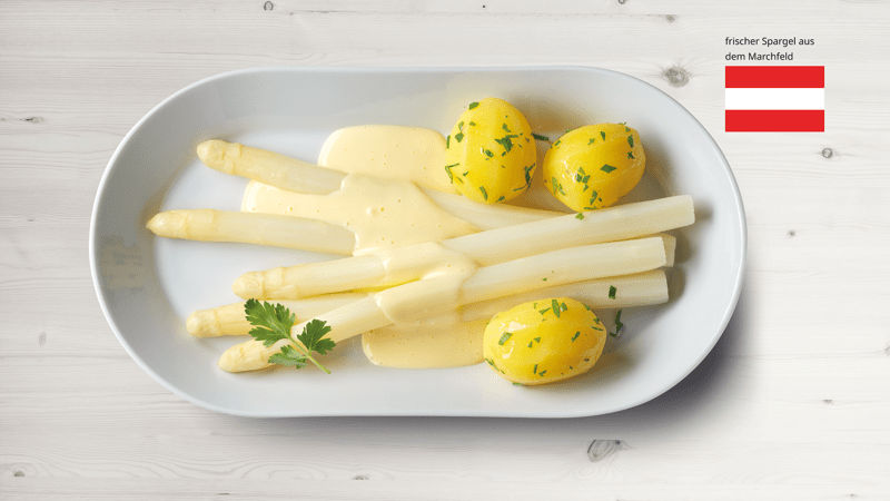 Spargel mit Kartoffeln und Sauce Hollandaise auf einem Teller präsentiert.