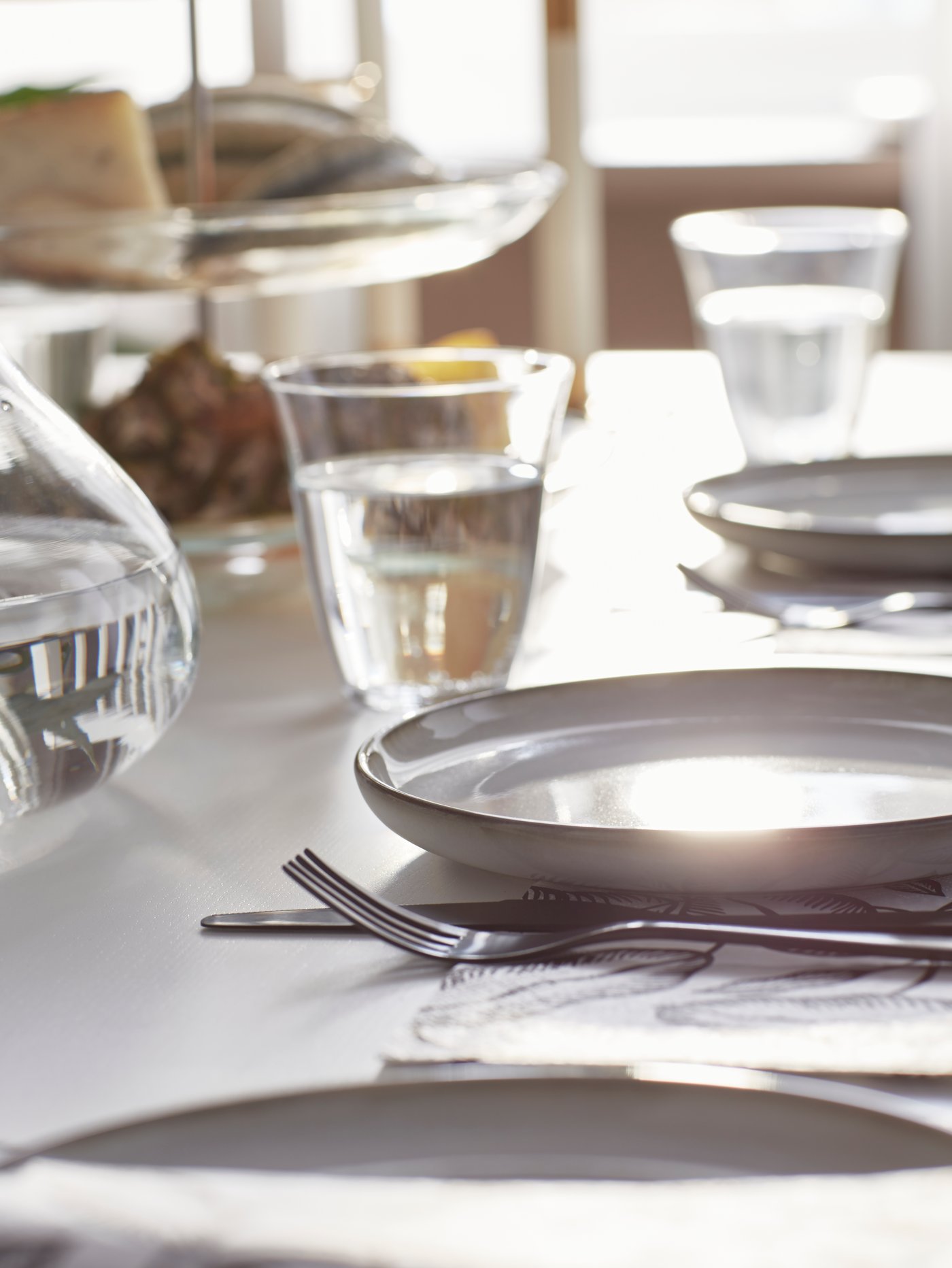 Personne tenant un bol de nourriture GLADELIG au-dessus d’une assiette GLADELIG grise, sur une table FRIDNÄS.