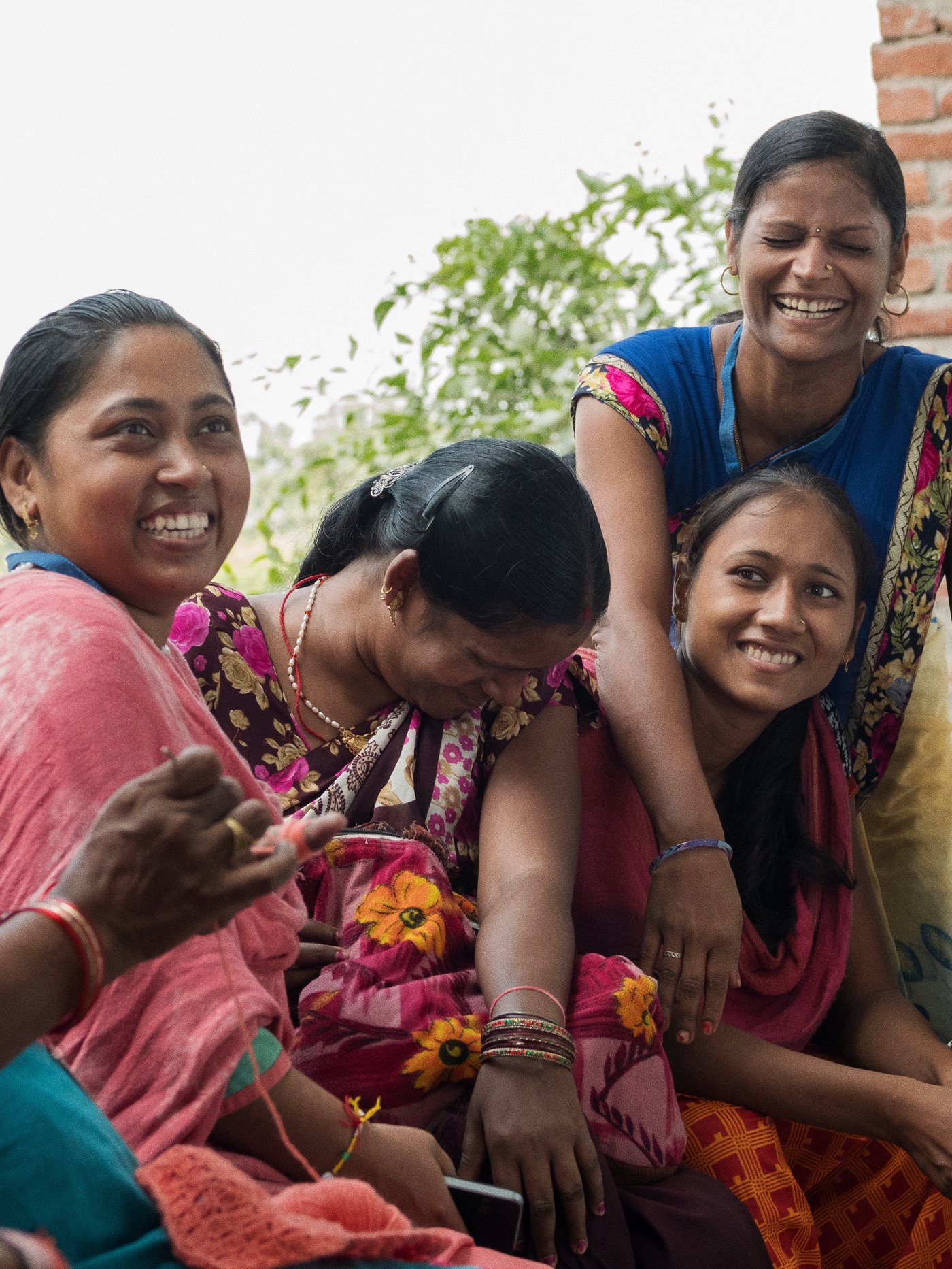 Four Indian weavers in brightly coloured traditional dress and jewellery, enjoying a laugh outside.