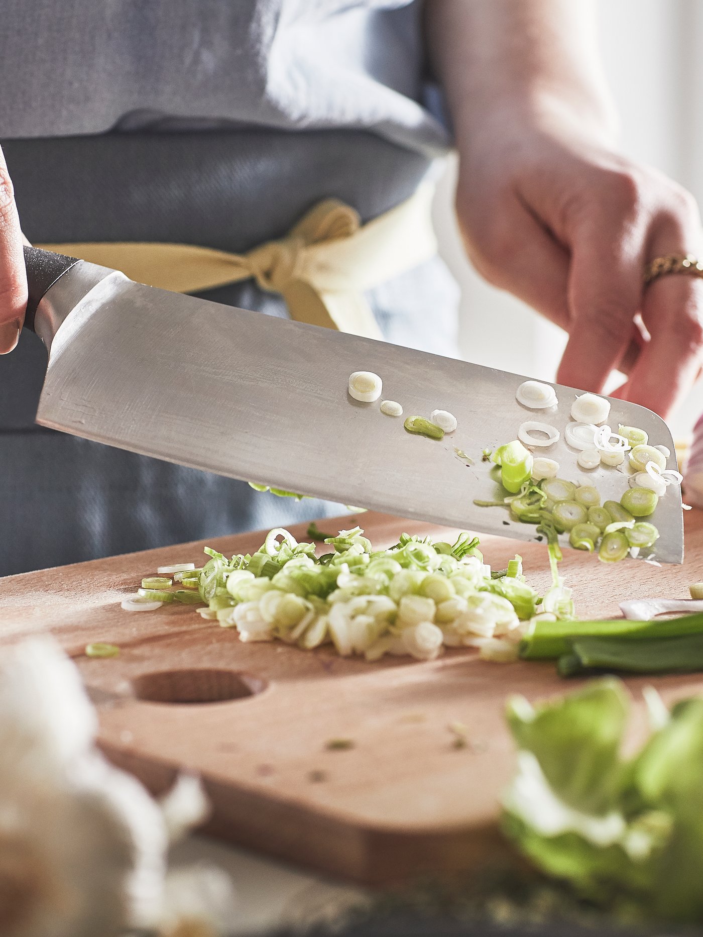 A person wearing a grey apron is chopping spring onions on a chopping board using a VÖRDA chinese chopper.
