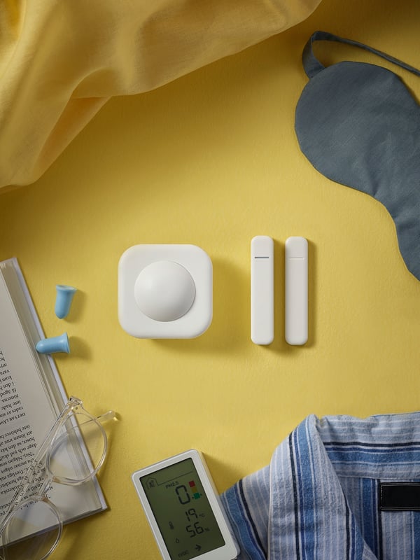 A VALLHORN wireless motion sensor and PARASOLL door/window sensor on a floor in the centre of everyday bedtime items.