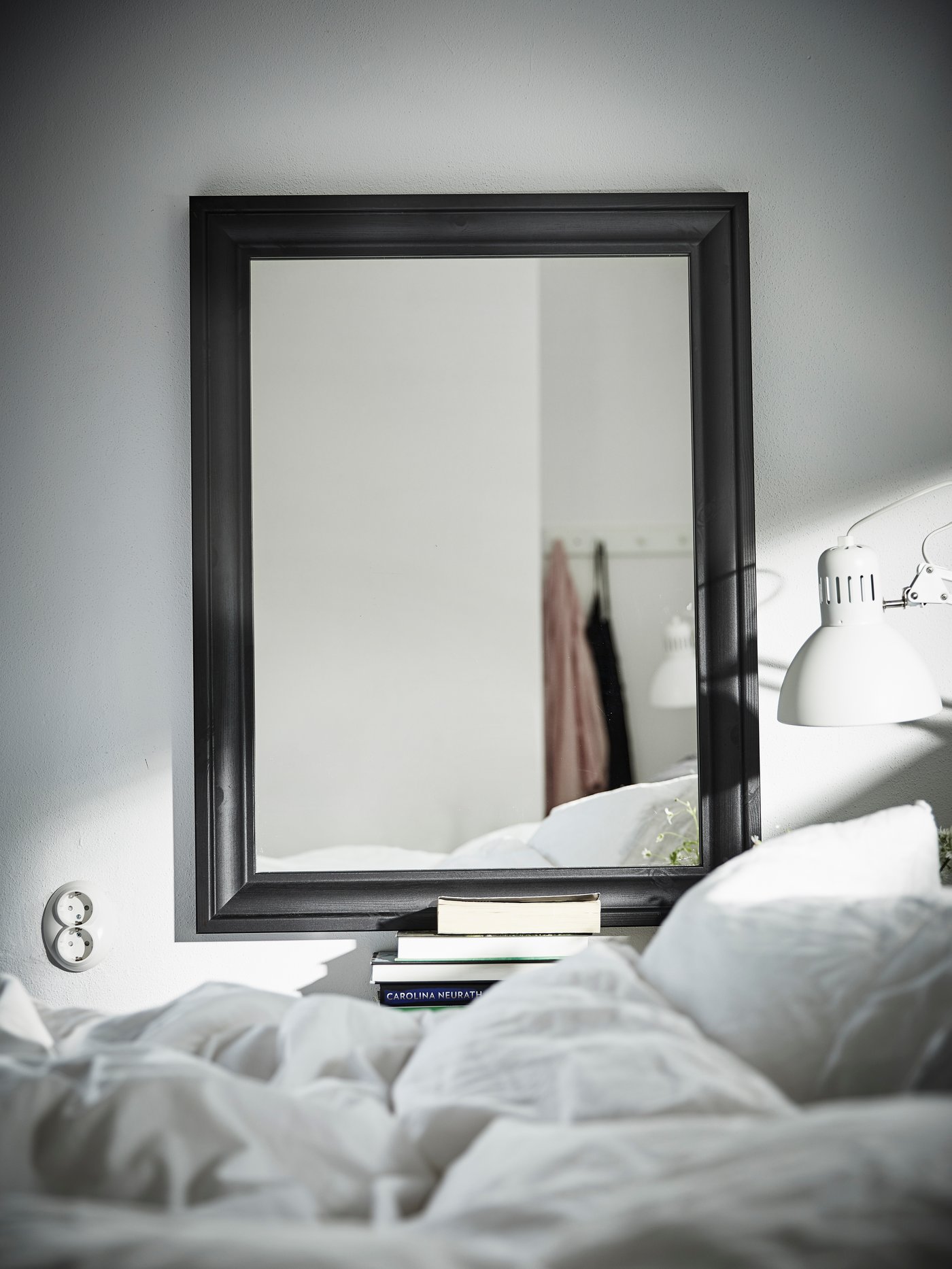 Un espejo TOFTBYN negro al costado de una cama con ropa de cama de algodón blanca.