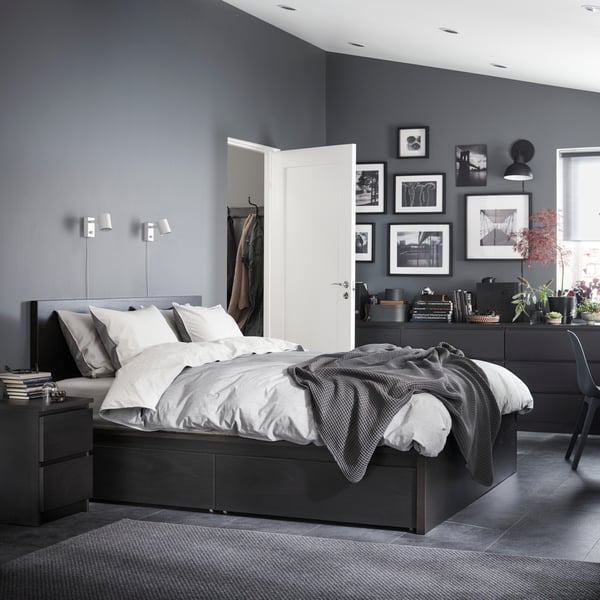 Ein Hotelzimmer in Grautönen eingerichtet mit einem schwarzen Doppelbett und Bildern an den Wänden