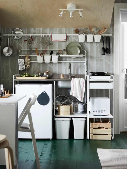 A SUNNERSTA unit kitchen against a grey wall with rails holding utensils, plates, and saucepans and a frying pan on the hob.
